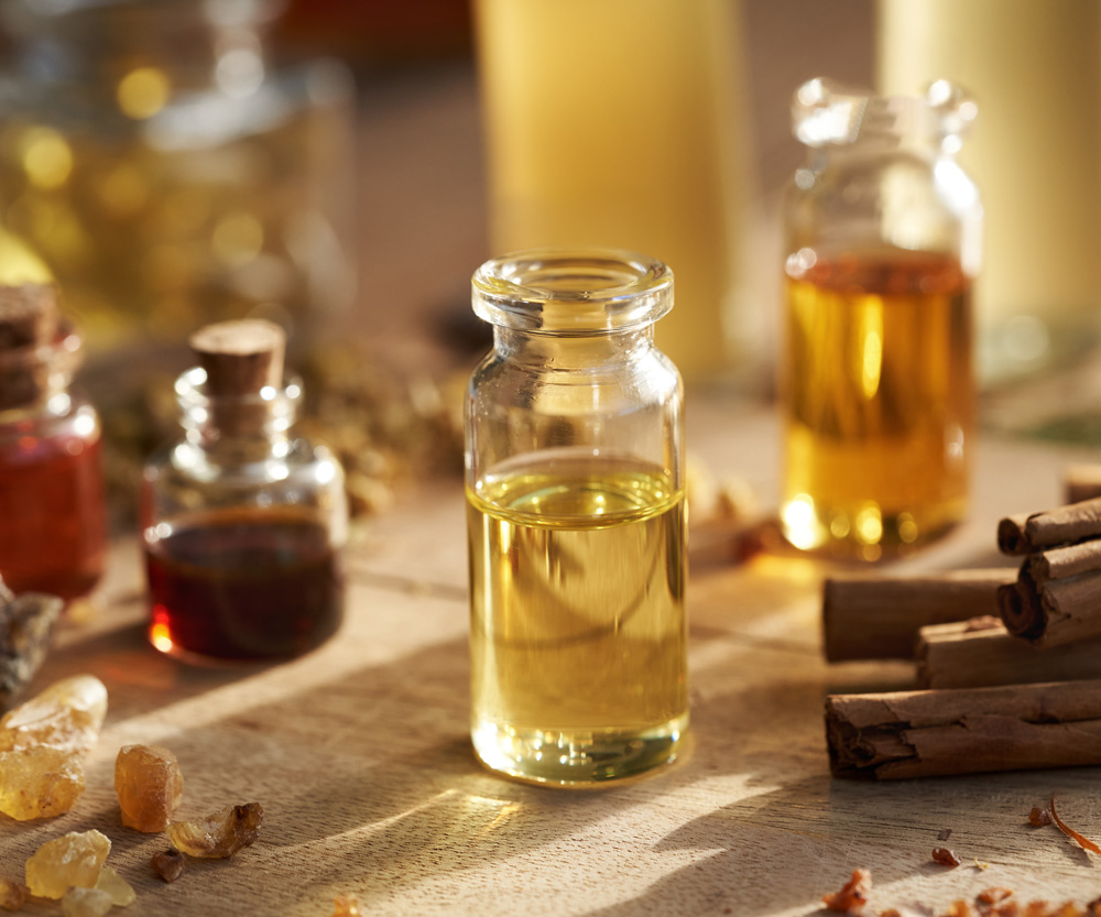 Essential Oil on table surrounded by cinnamon, black pepper , olibanum etc